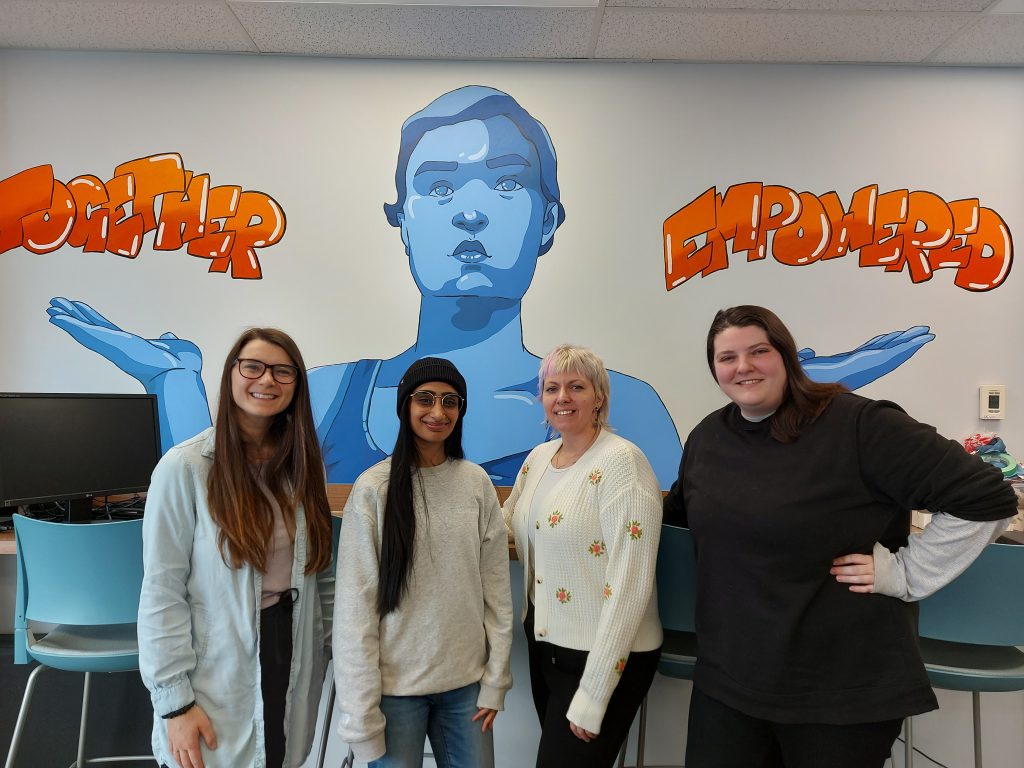 Chelsea Klassen, Imran Tatla, Frankie Fowle, and Carlanna Thompson stand together under a Together Empowered sign