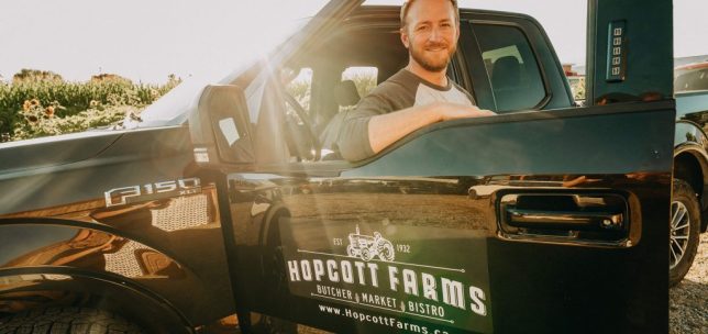 Travis Hopcott standing beside a pickup truck with the sunset behind him.