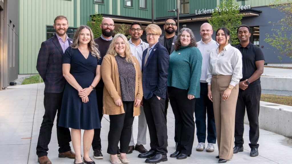 UFV alumni association board members posing for a group photo in front of the student housing building on the Abbotsford campus.